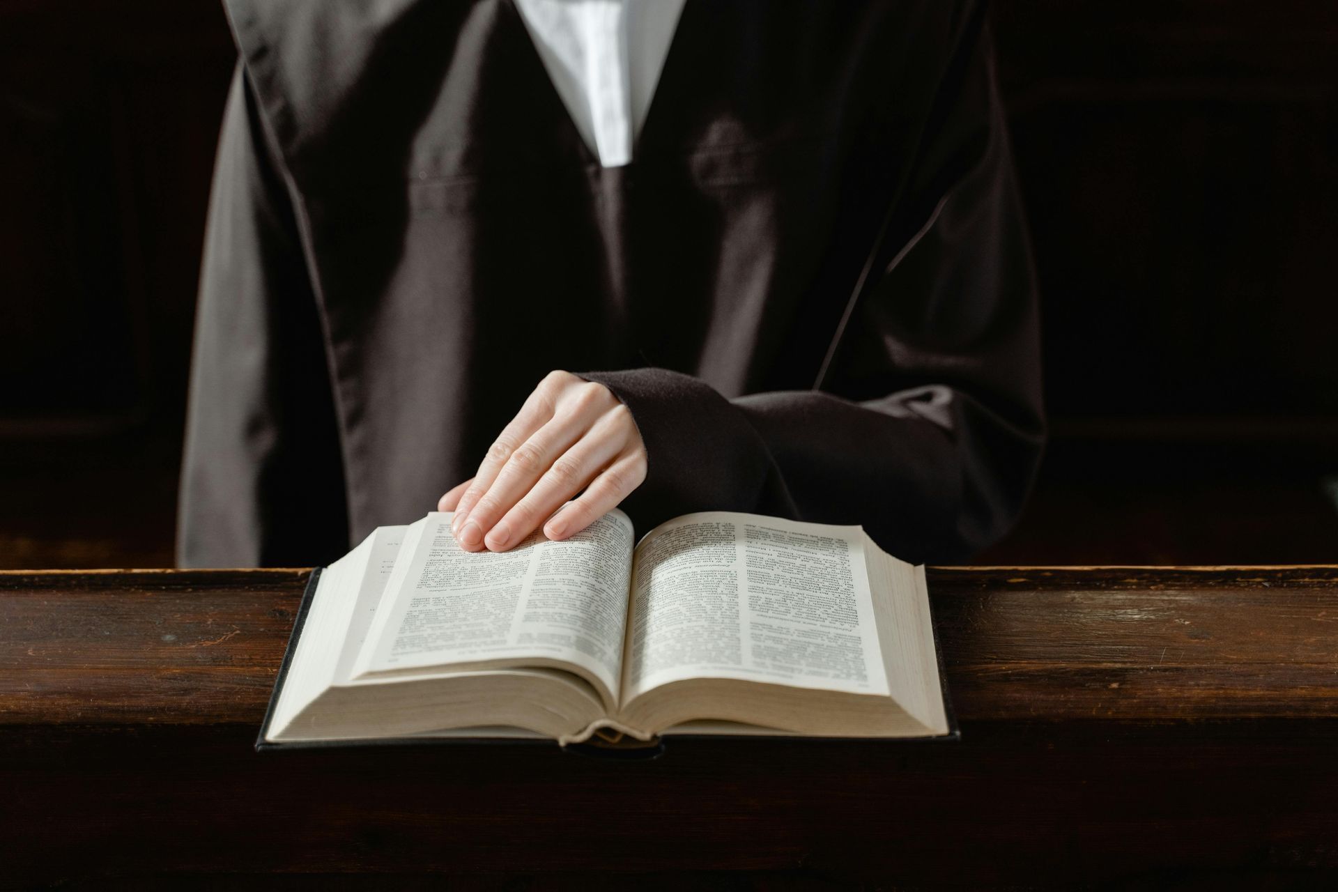 Person in black robe, hand on an open book, likely taking an oath.