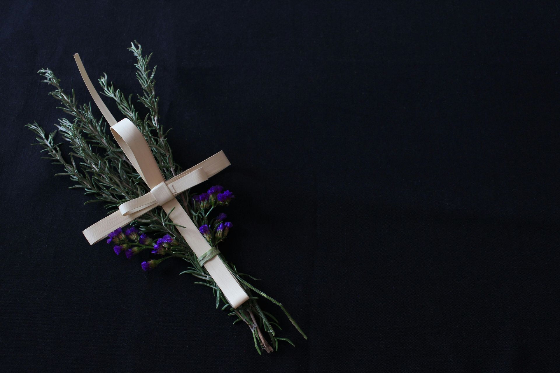 Palm cross with herbs and purple flowers against a dark background.