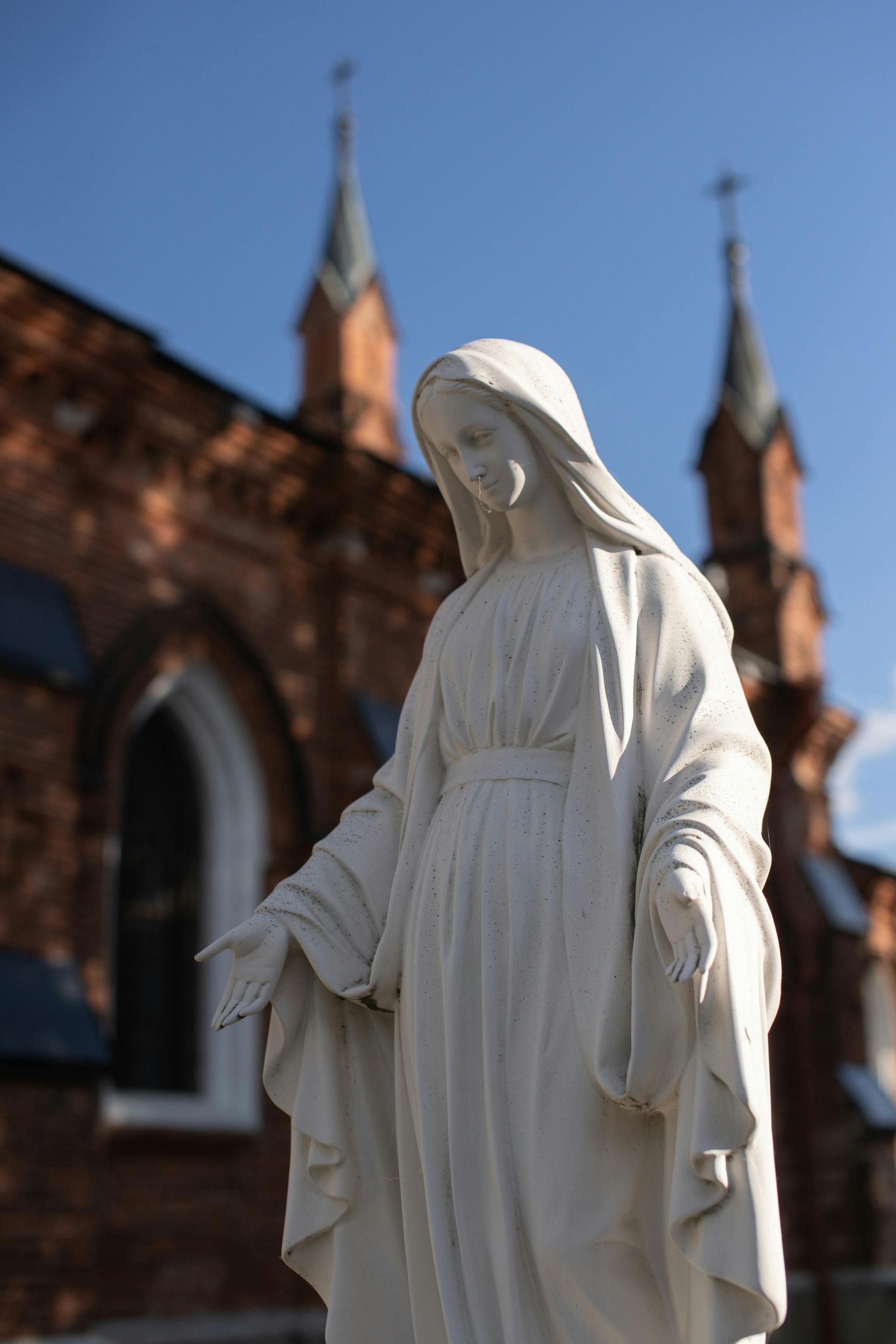 Statue of Virgin Mary in front of a red brick church with two spires.