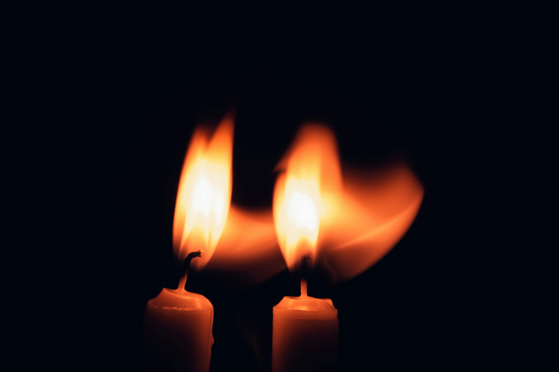 Two lit candles with orange flames against a dark background.