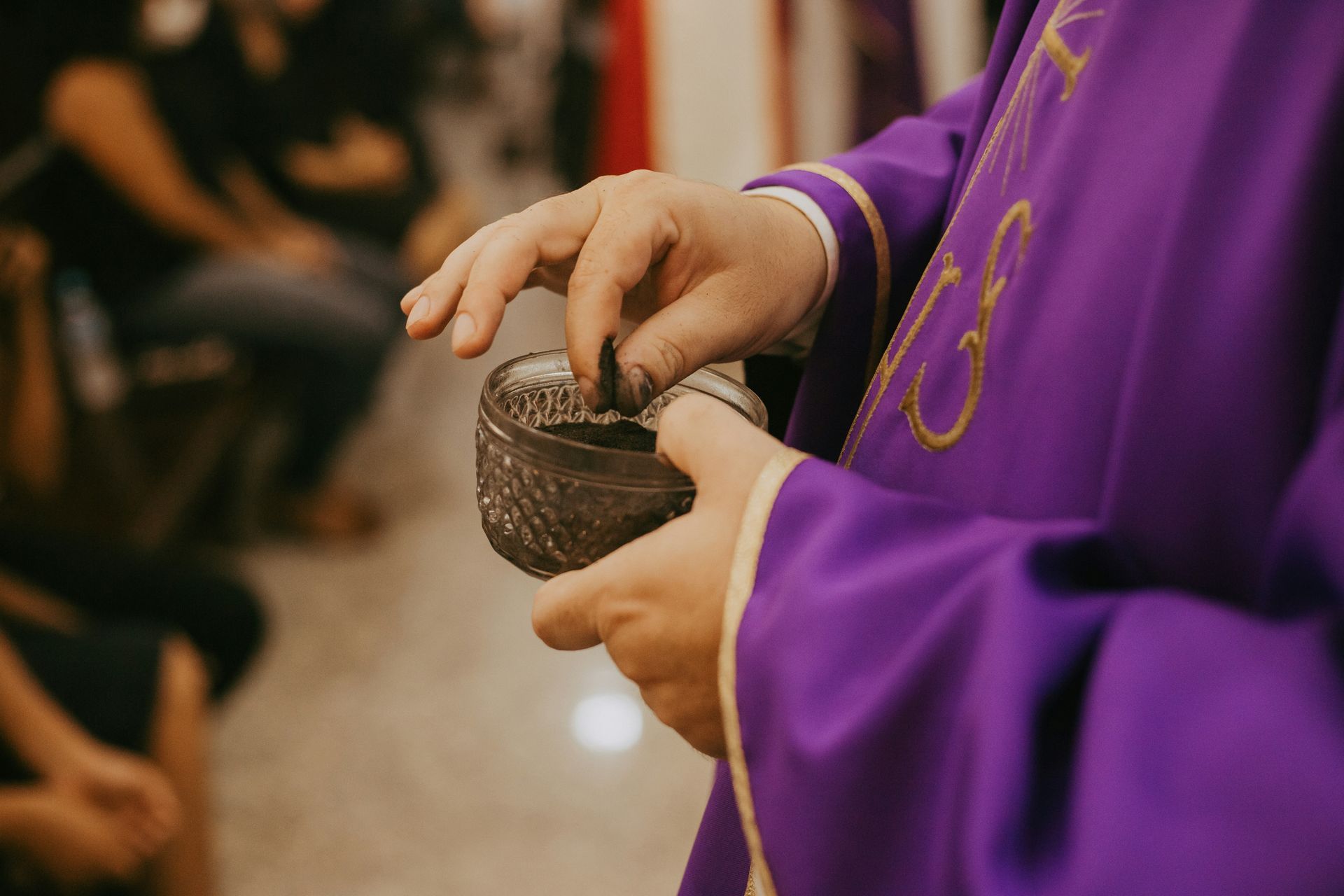 Person in purple robe holding a bowl of ashes, preparing to apply them during a religious ceremony.