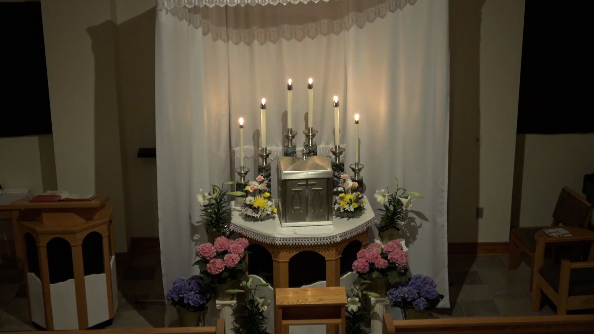 Altar with tabernacle surrounded by 7 candles with a drape background and flowers