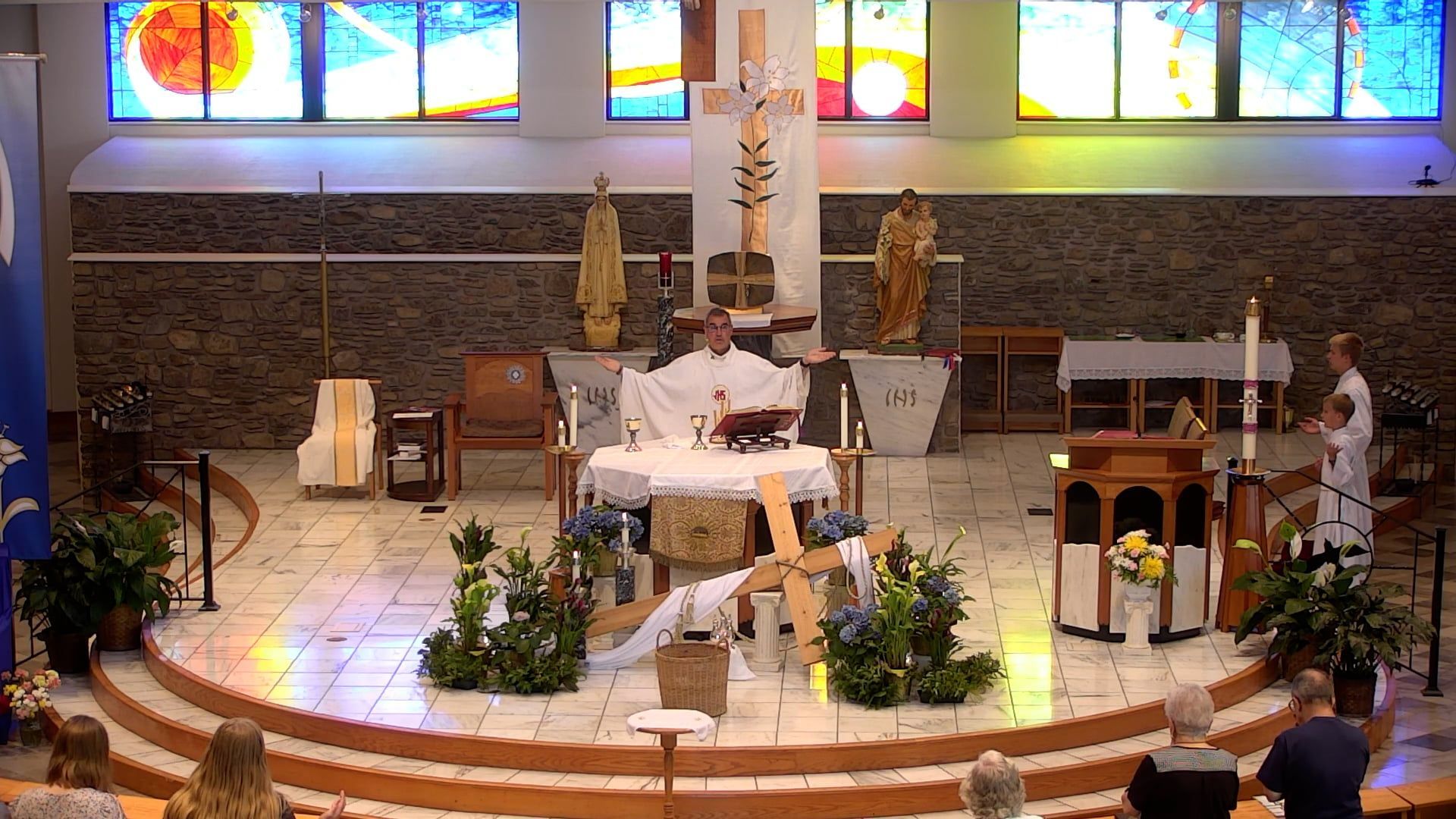 Fr. Pete in the church with a stained glass window behind the altar celebrating mass