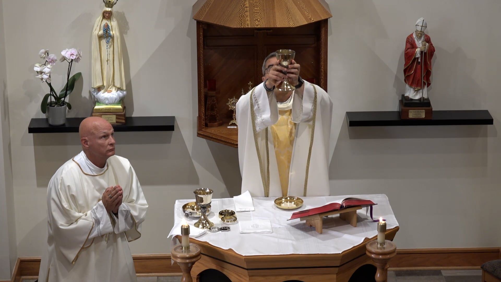Fr. Pete standing at an altar in the chapel holding the chalice up in the air.