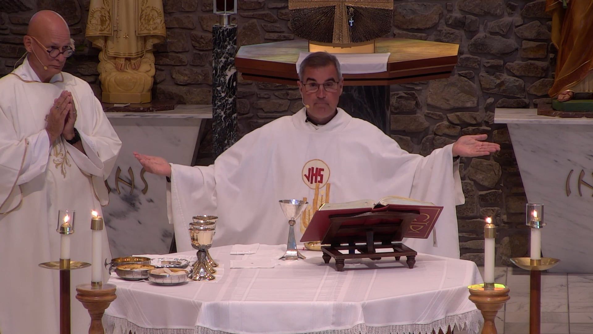 Father Pete holding his arms out with Deacon Bill at the altar in the main church. 