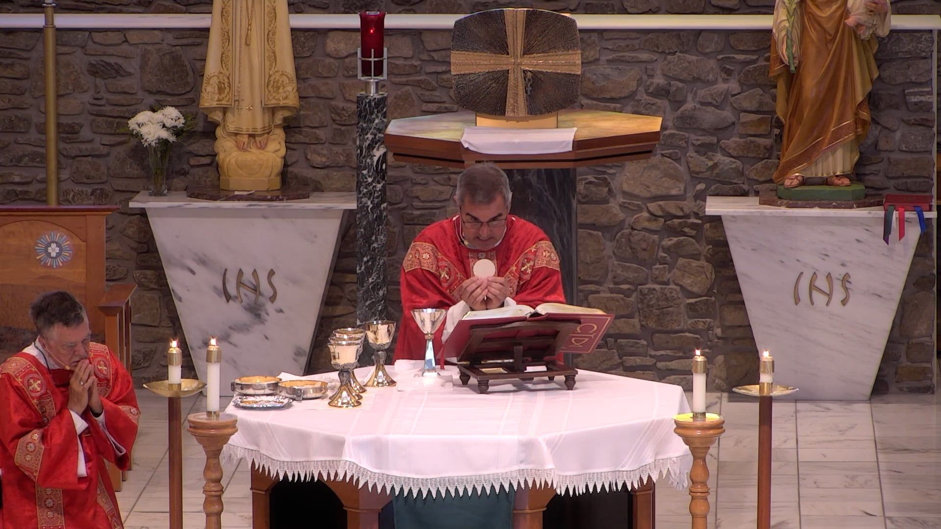 Fr. Pete holding the eucharist and Deacon Leon kneeling celebrating mass in the main church
