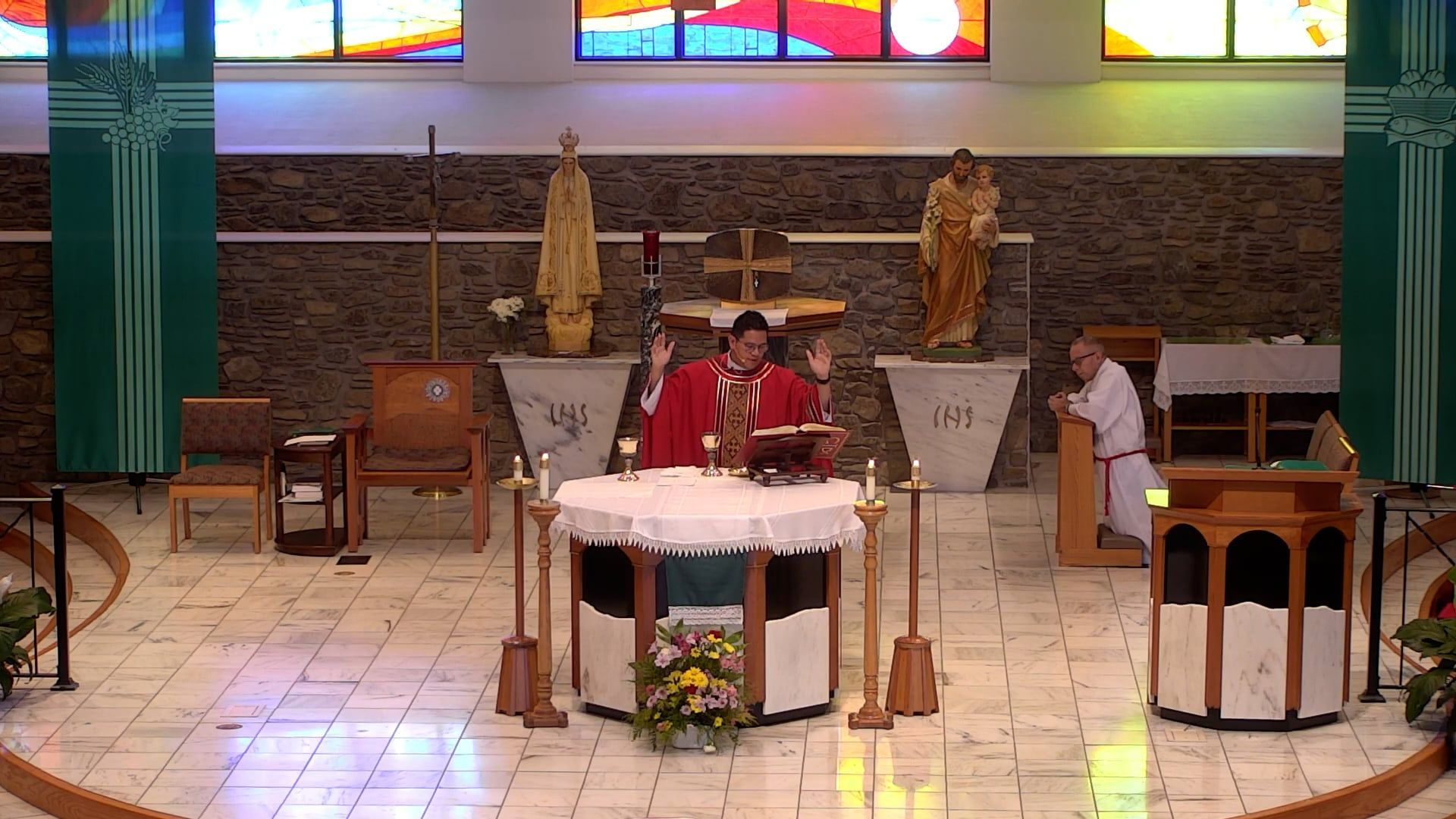 Father Renzo with his arms raised at the altar in the main church celebrating mass. 