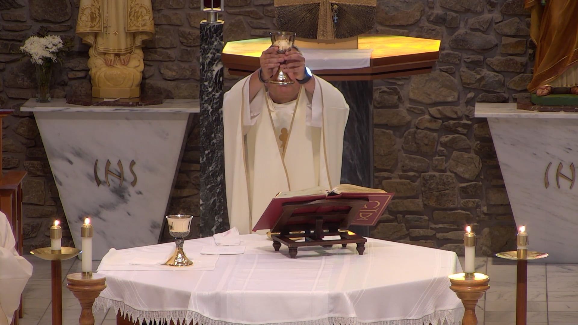 Father Pete holding up the chalice in the main church celebrating mass that the altar. 