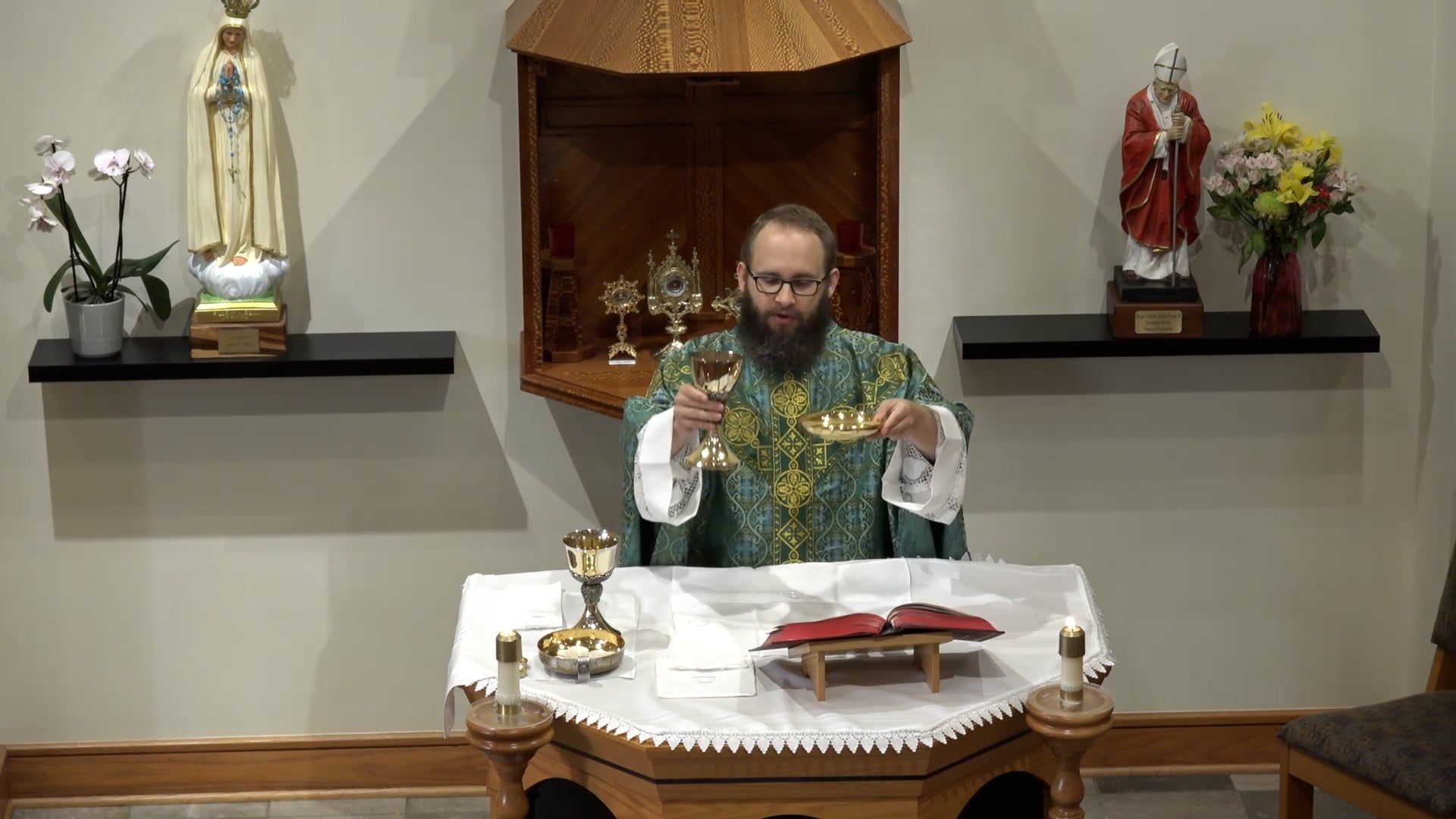 Fr. Joe holding the chalice up in the air at the altar in the chapel celebrating mass. 