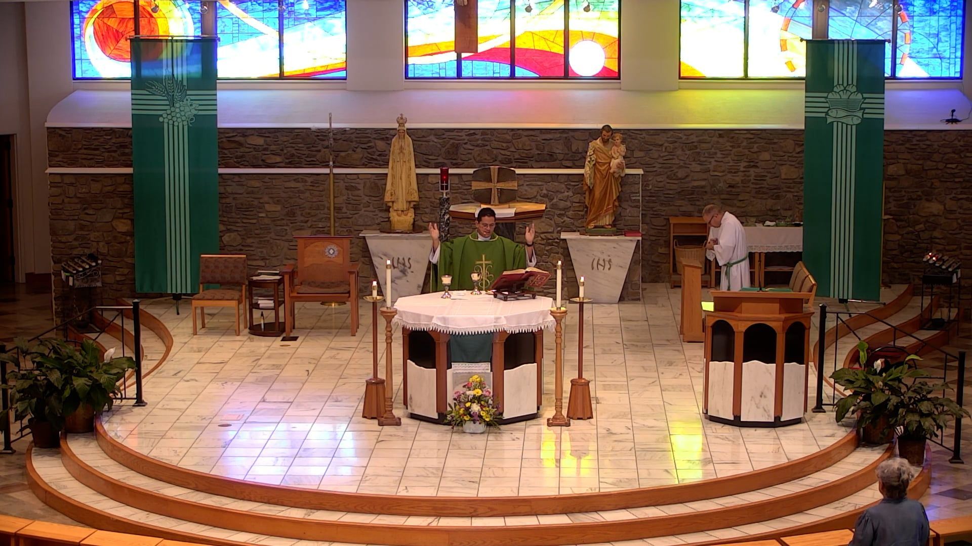 Father Renzo at the altar with his hands raised in the main church with the sun streaming in