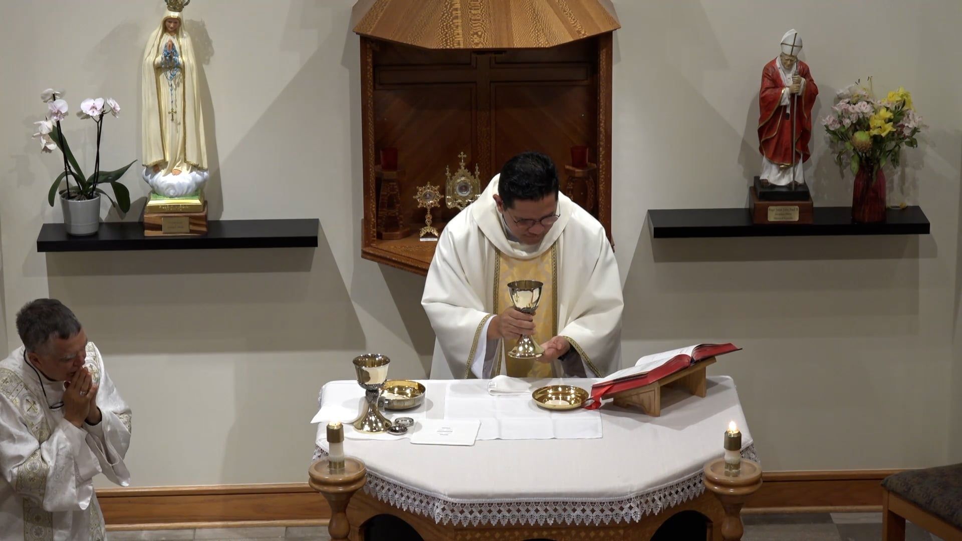 Fr. Renzo holding the chalice in the chapel at the altar with Deacon Leon kneeling beside. 