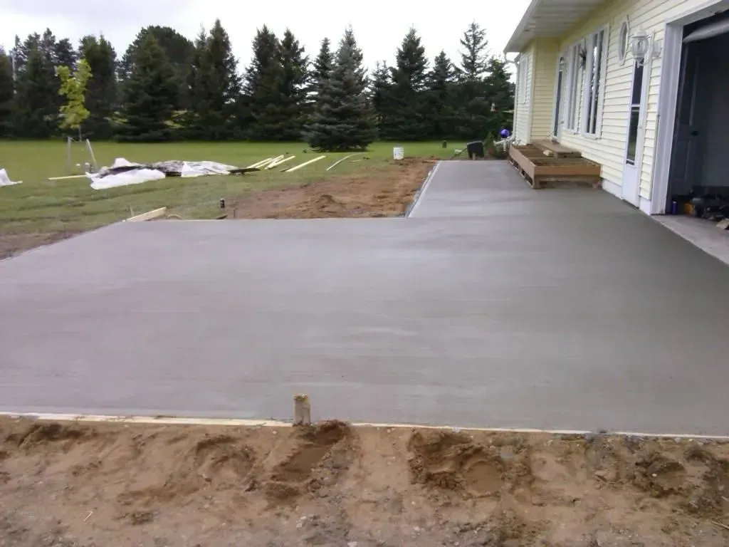 Freshly poured concrete patio beside a house with a yard and trees in the background