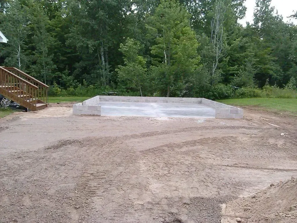 Empty concrete pad in a dirt clearing with trees and a wooden staircase at left
