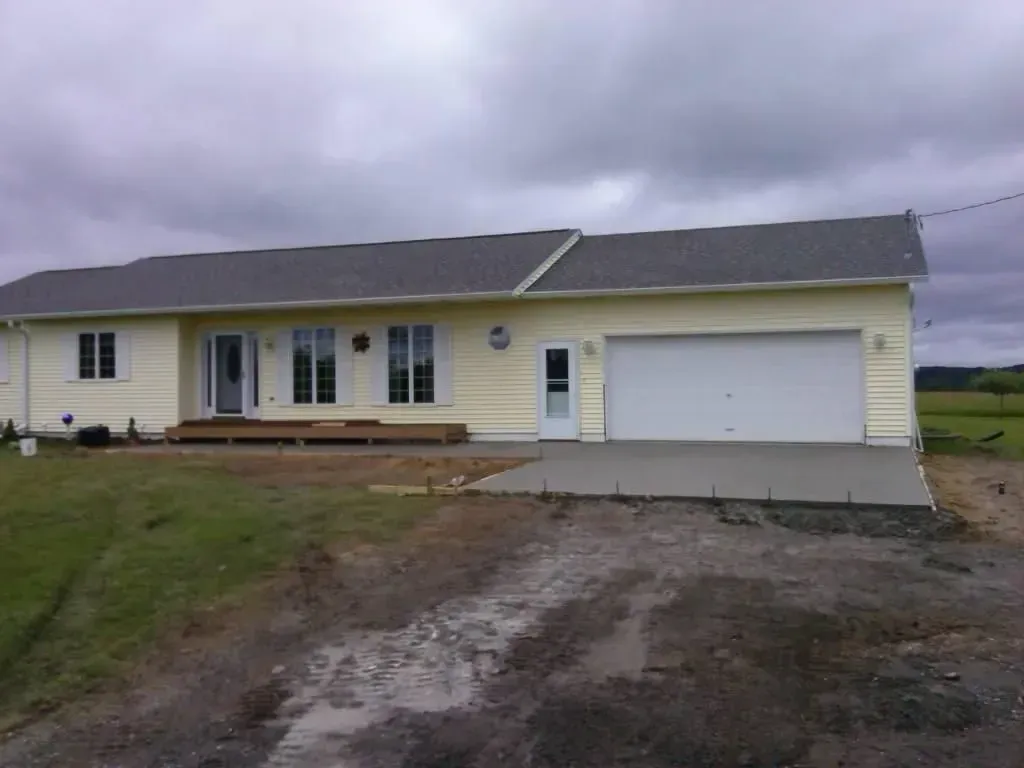 Single-story yellow house with white garage and muddy driveway under cloudy sky