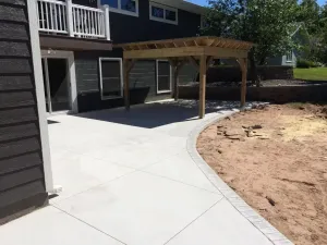 Backyard patio with a curved concrete path, pergola, and house deck beside a dirt landscaping area
