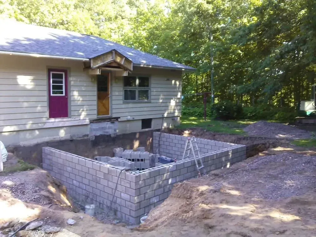 House with a newly built cinder block foundation pit and dirt yard surrounded by trees