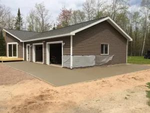 Brown house with attached garage and concrete driveway in a wooded rural setting