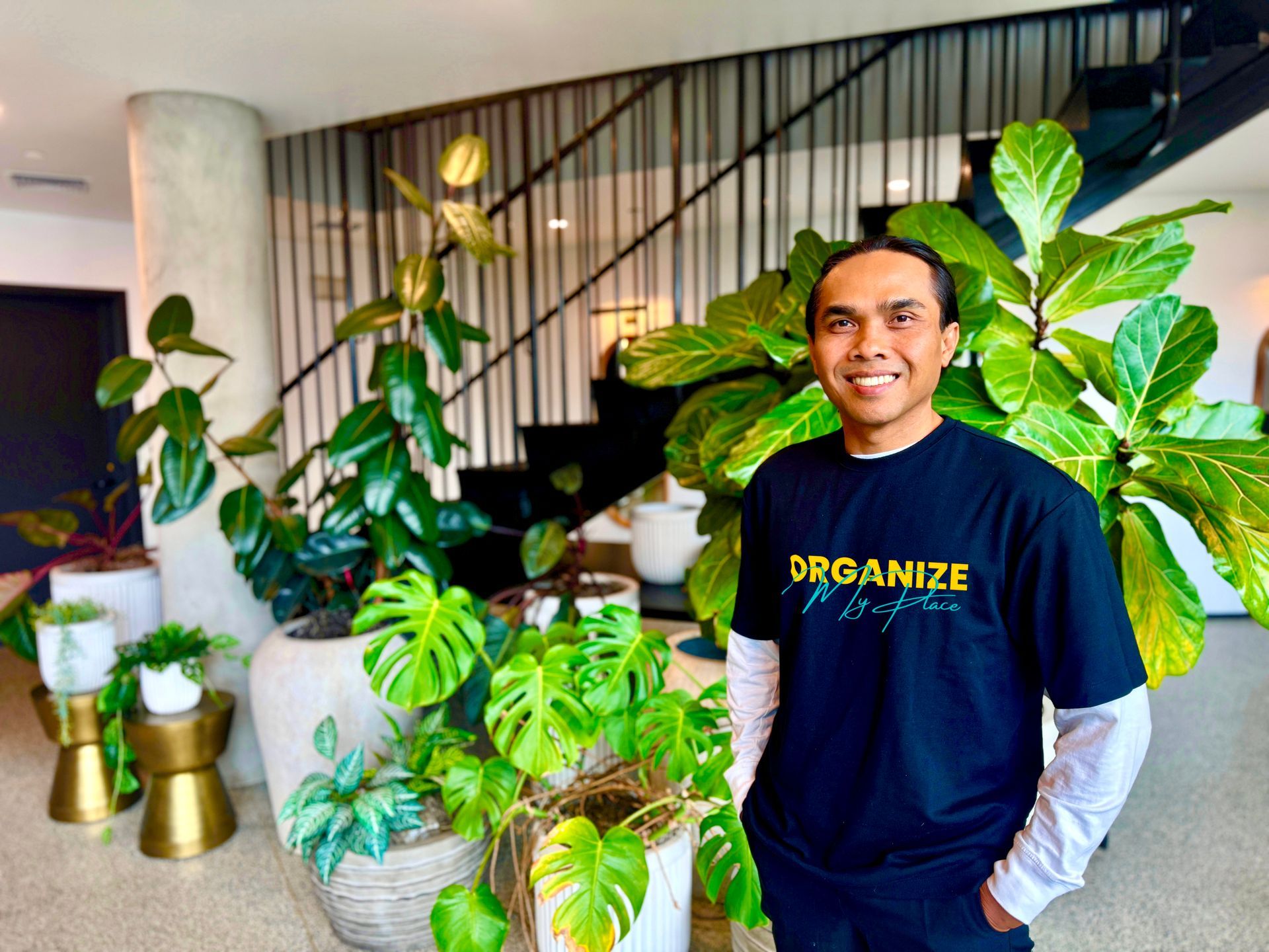 A man in a black shirt is standing in front of potted plants.