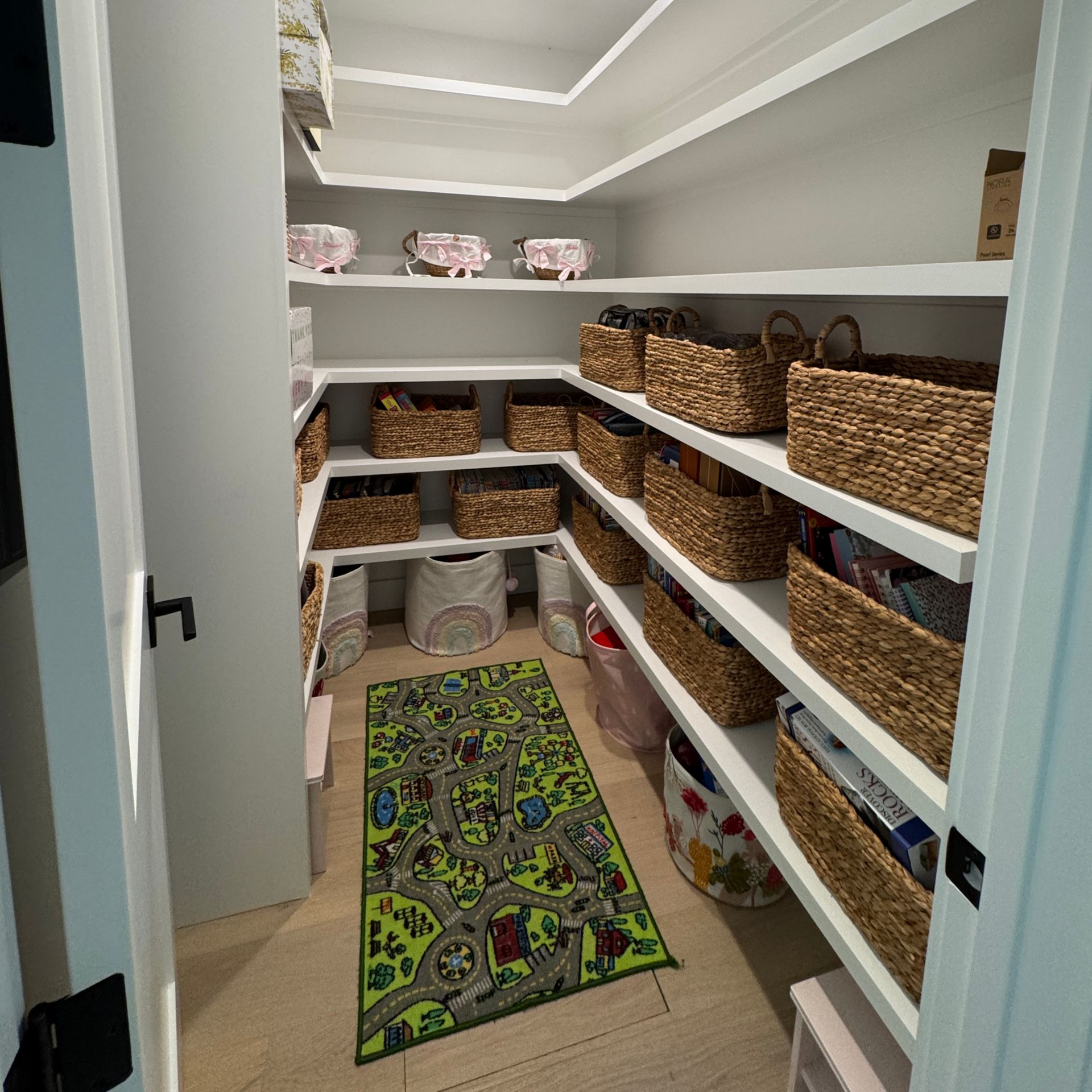 A well-organized pantry with shelves filled with baskets and containers, a colorful rug on the floor.
