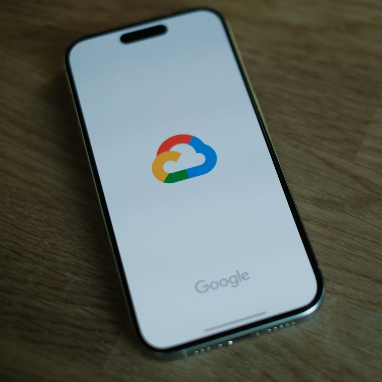 Smartphone displaying the Google Cloud logo on its screen, resting on a wooden surface.