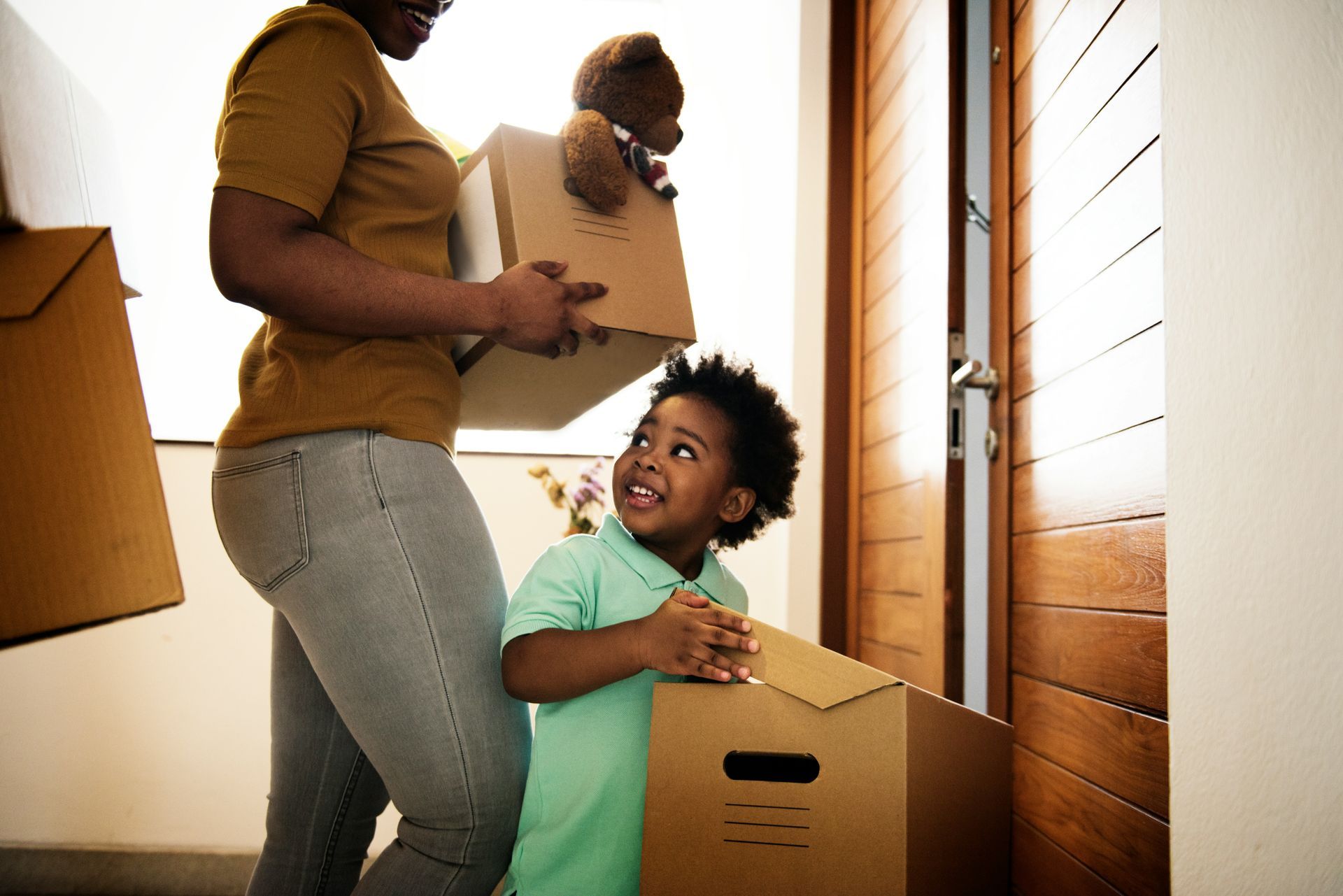 A woman is carrying a cardboard box and a child is holding a cardboard box.