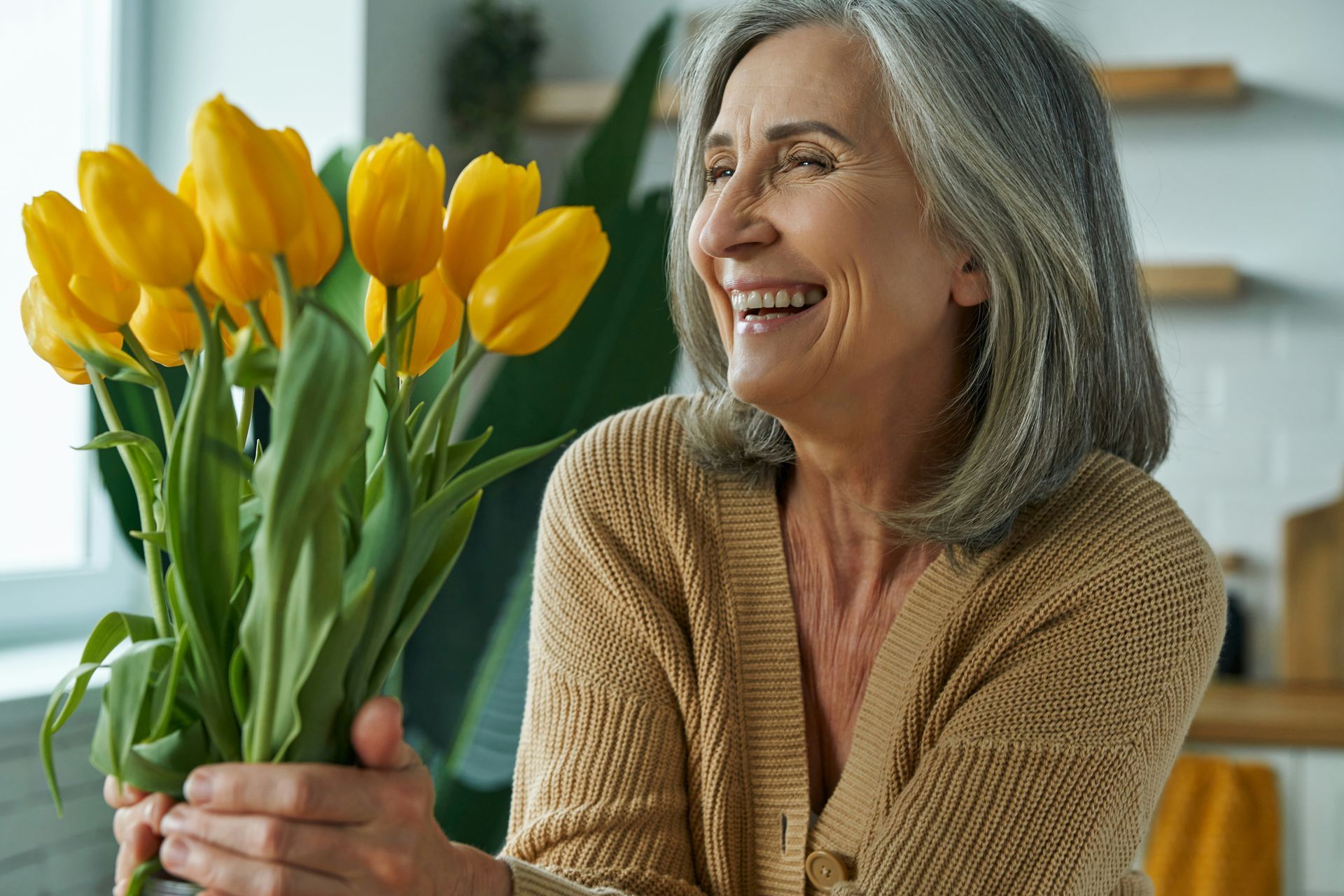 An elderly woman is holding a bouquet of yellow tulips.