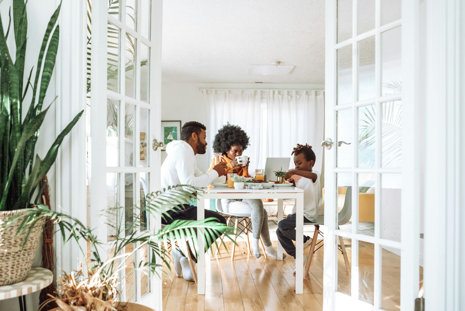 A family is sitting at a table in a living room with a laptop.
