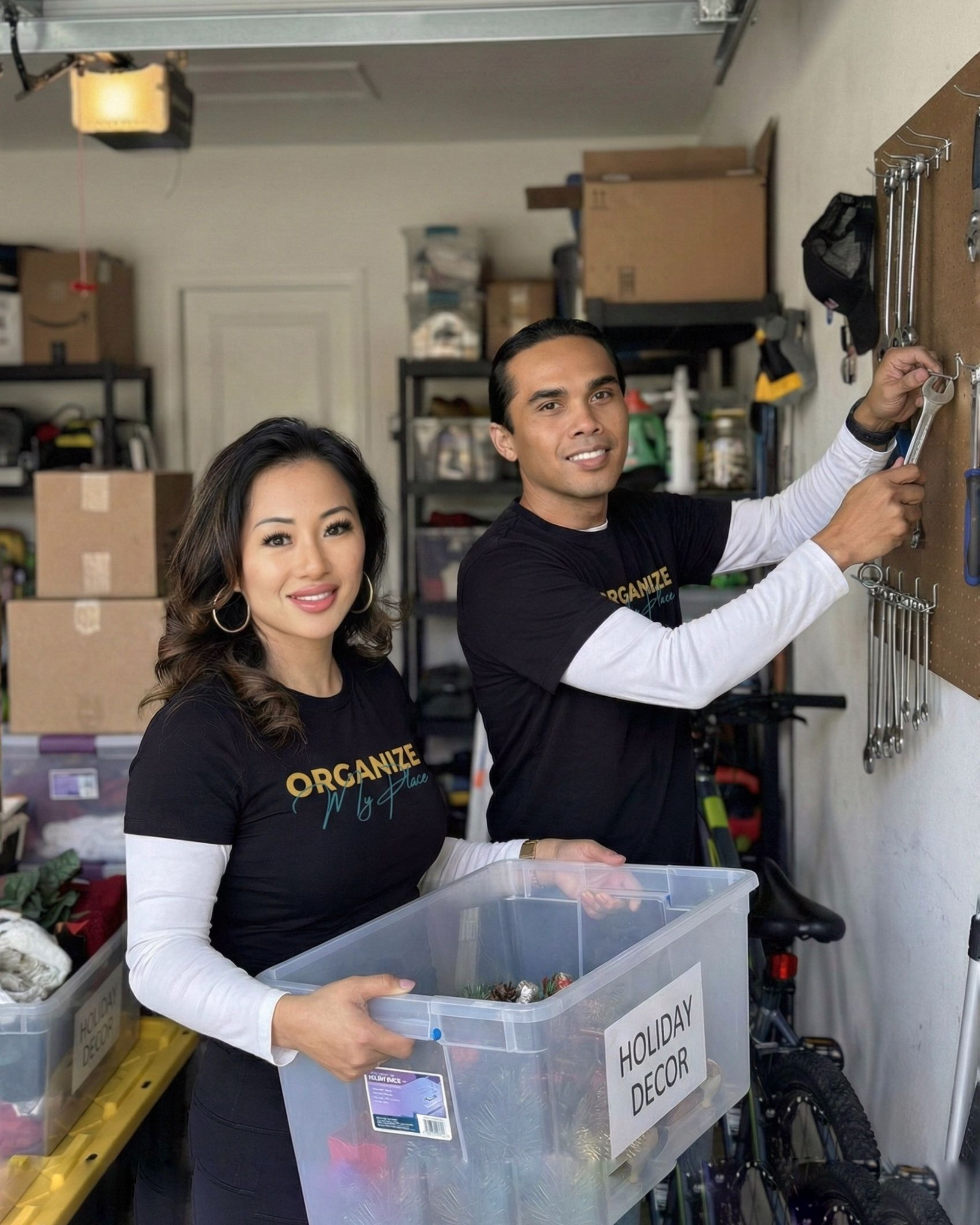 Two people organizing a garage; one holding a bin, the other hanging tools. Both wearing matching shirts.