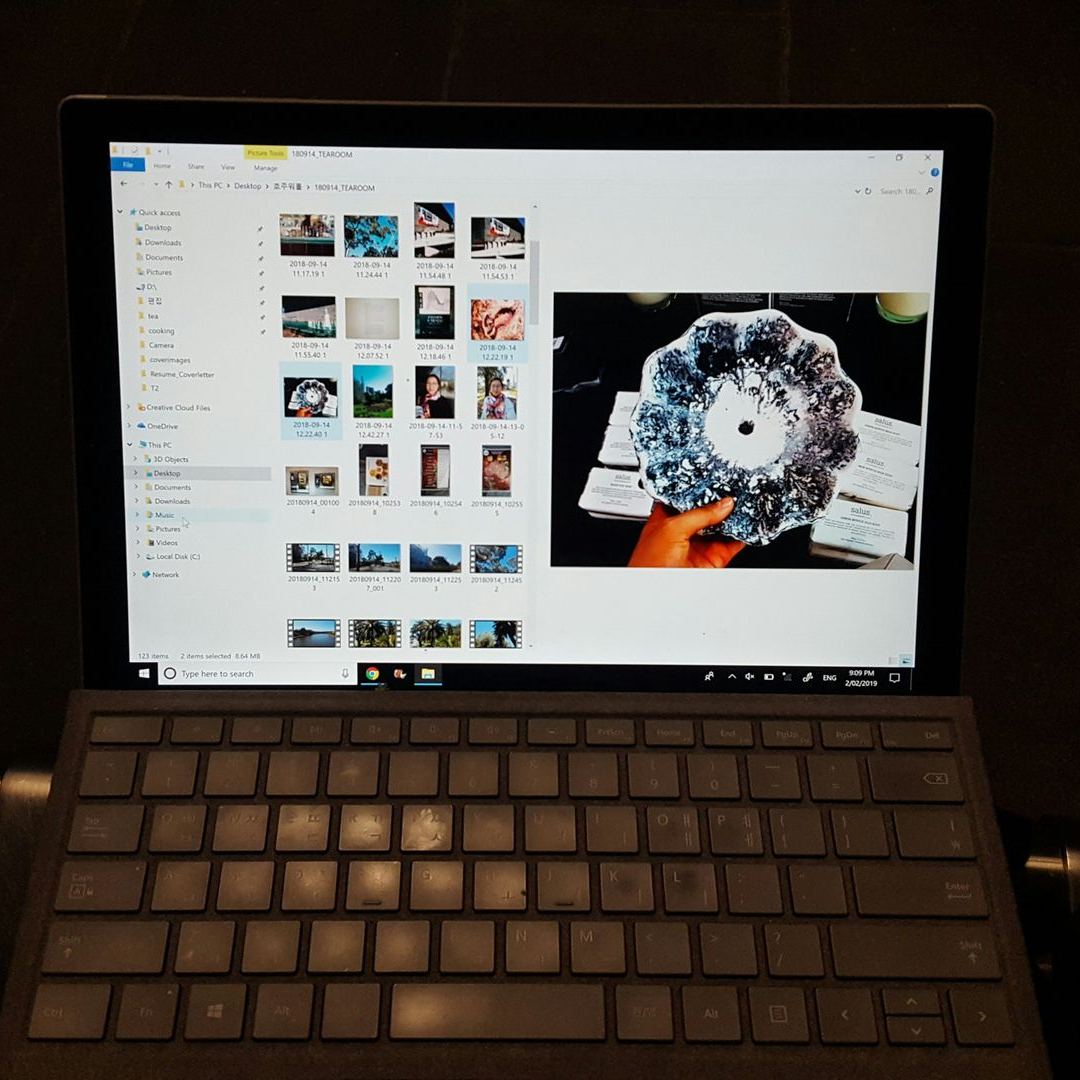 Laptop screen displaying a file explorer with photos and a close-up of a hand holding a decorative item.
