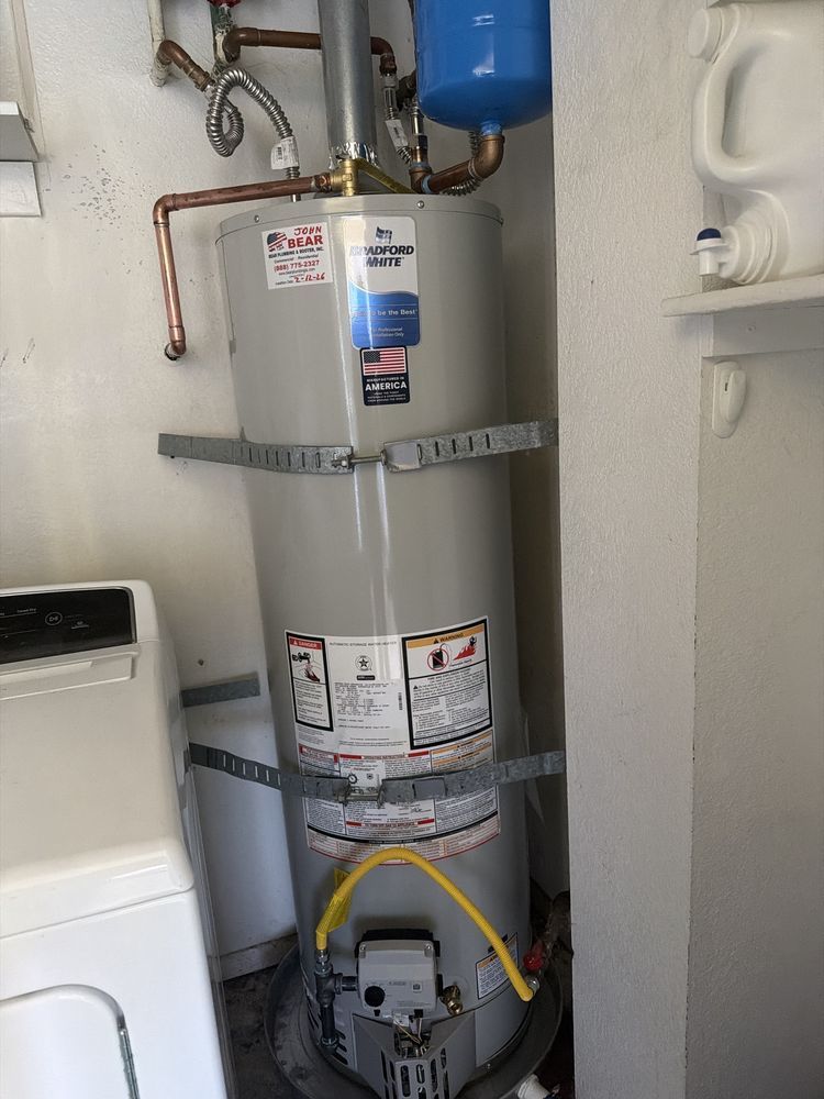 A gray water heater with seismic straps stands in a utility closet next to a white washing machine.