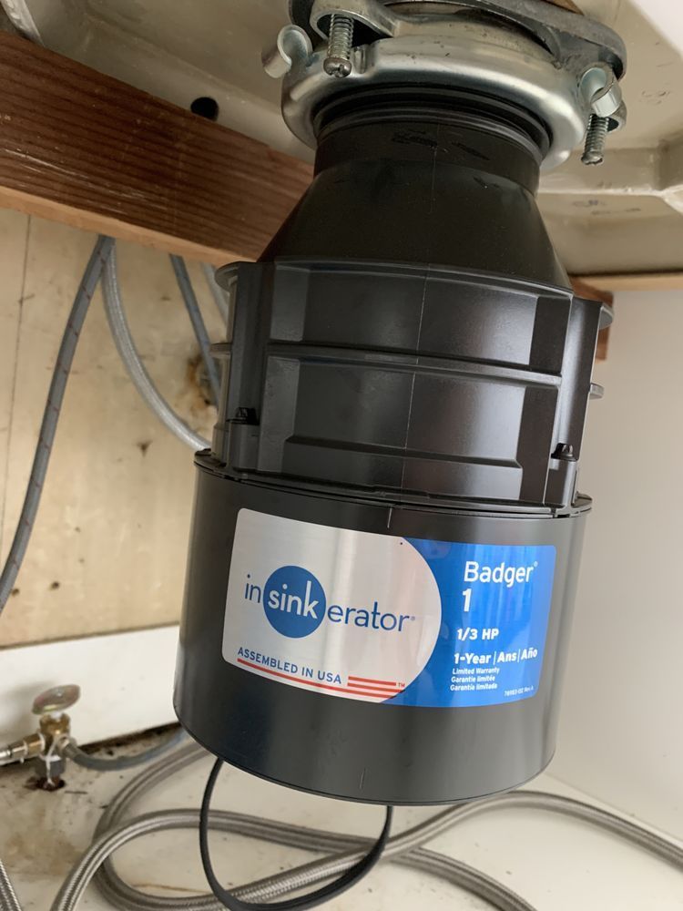 A black InSinkErator Badger 1 garbage disposal unit mounted beneath a kitchen sink.