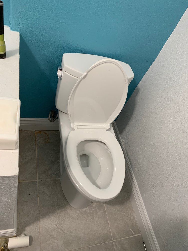 A white toilet with the lid open, positioned in a corner between a blue wall and a white wall on a gray tile floor.