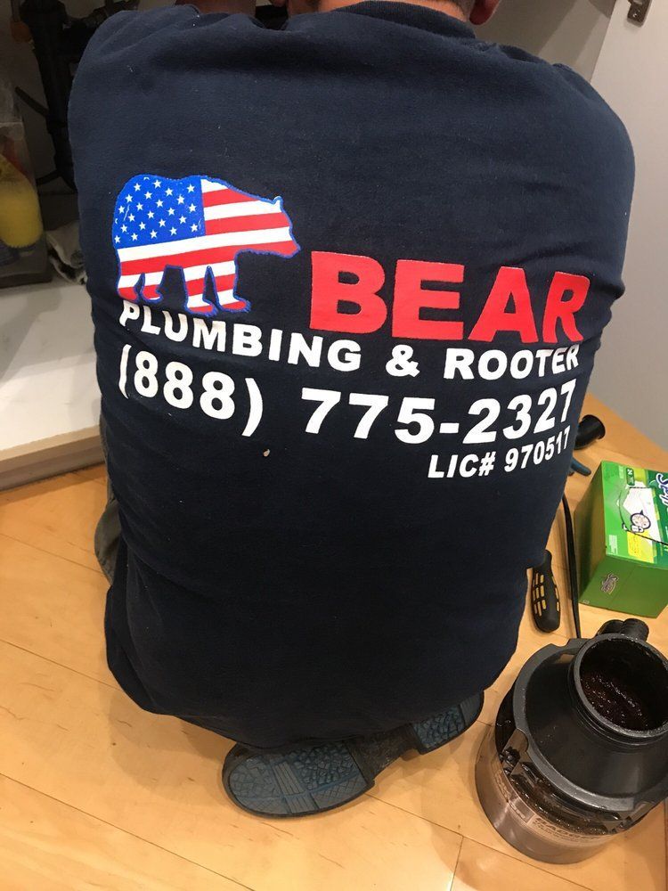 A plumber wears a dark navy shirt with a bear logo and