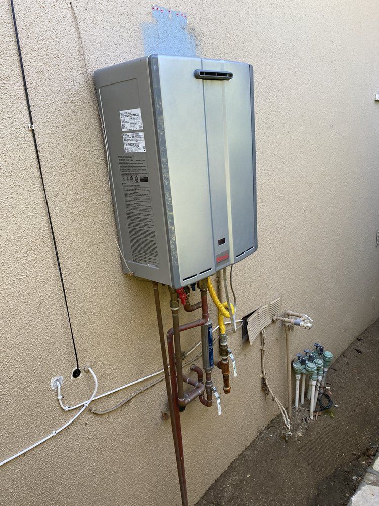 A tankless water heater mounted on an exterior stucco wall with copper and yellow gas piping below.