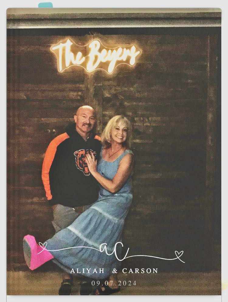 Couple posing for a photo. Wooden backdrop with neon
