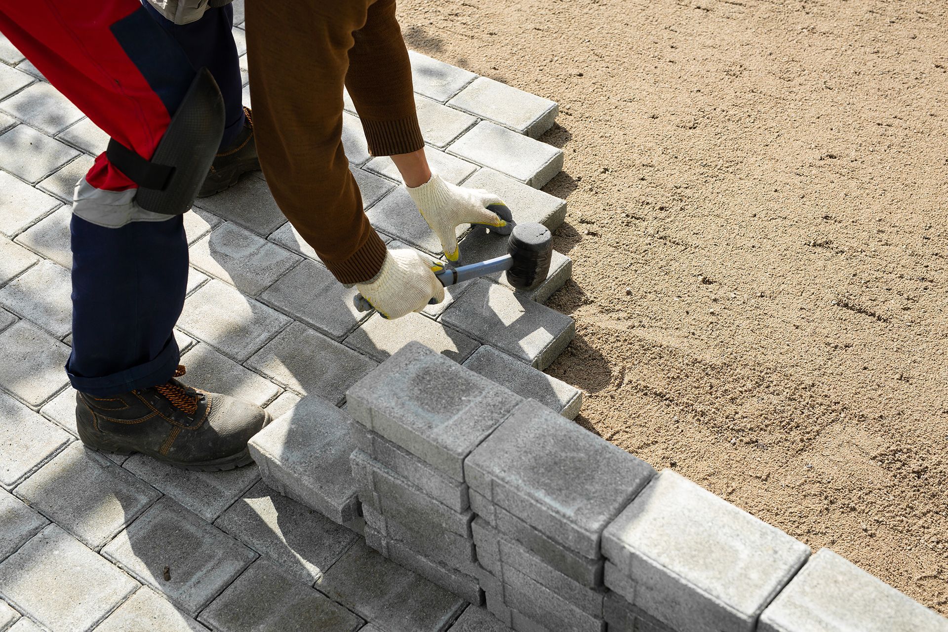 Person laying gray pavers on a gravel bed, using a mallet.