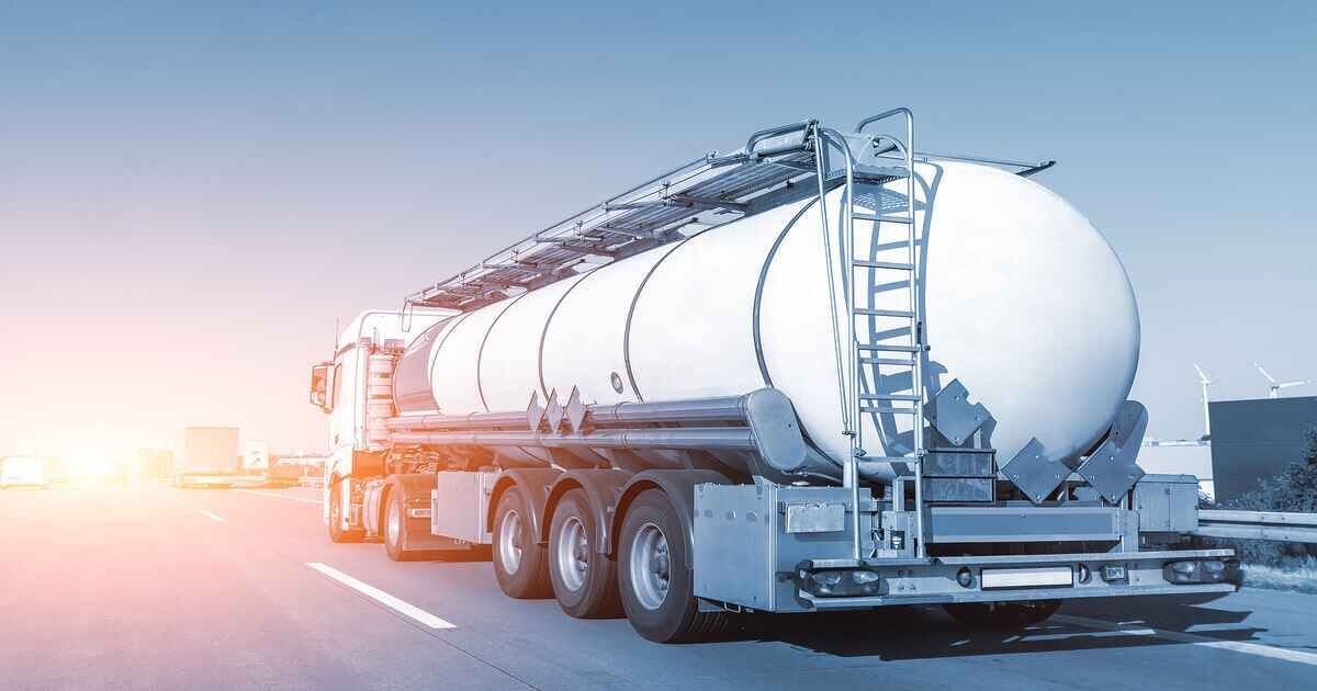 A tanker truck is driving down a highway at sunset.