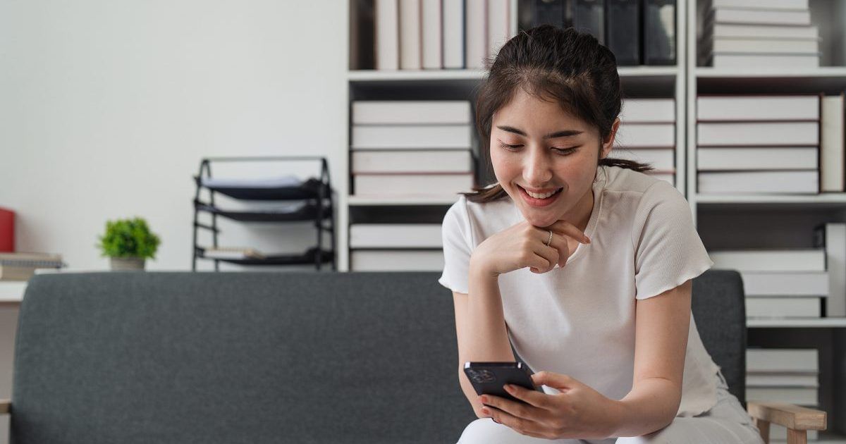 A woman is sitting on a couch looking at her cell phone.