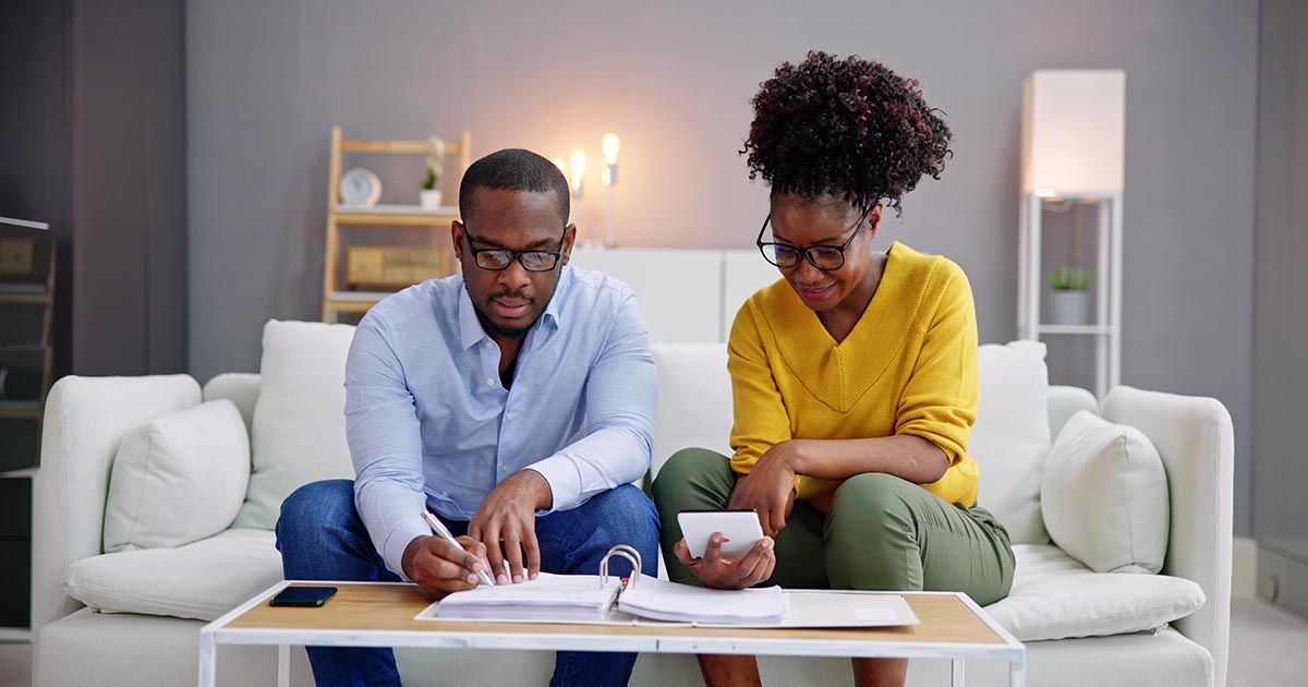 A man and a woman are sitting on a couch looking at papers.