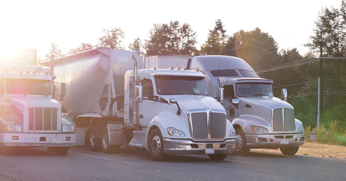 Three semi trucks are parked next to each other on the side of the road.