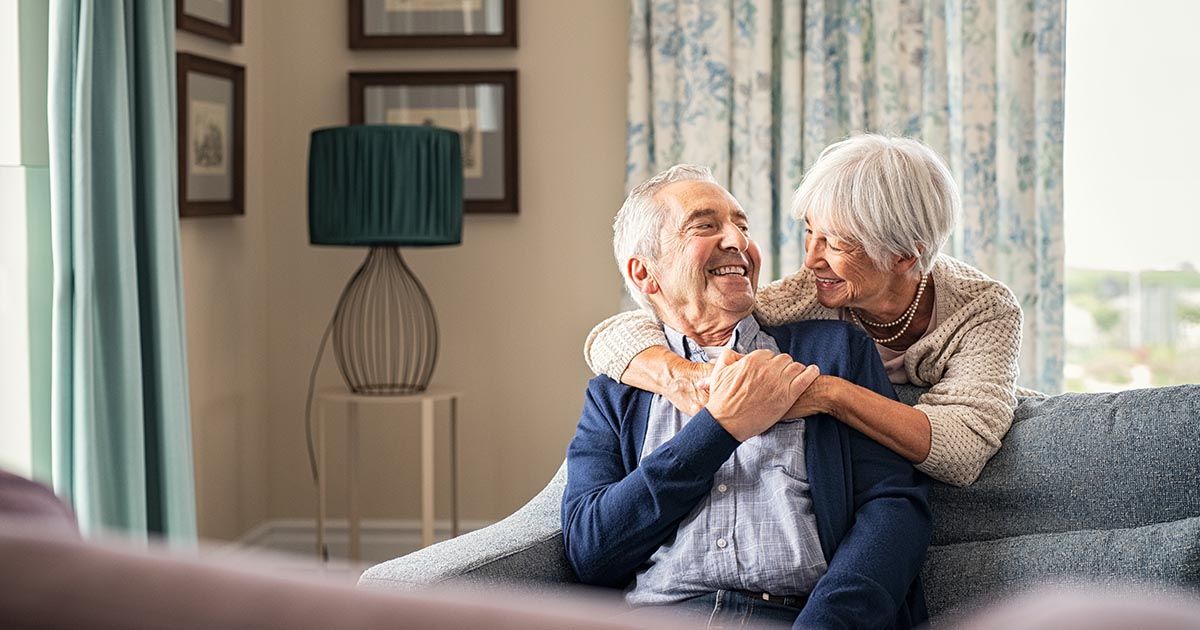 An elderly couple is sitting on a couch hugging each other.