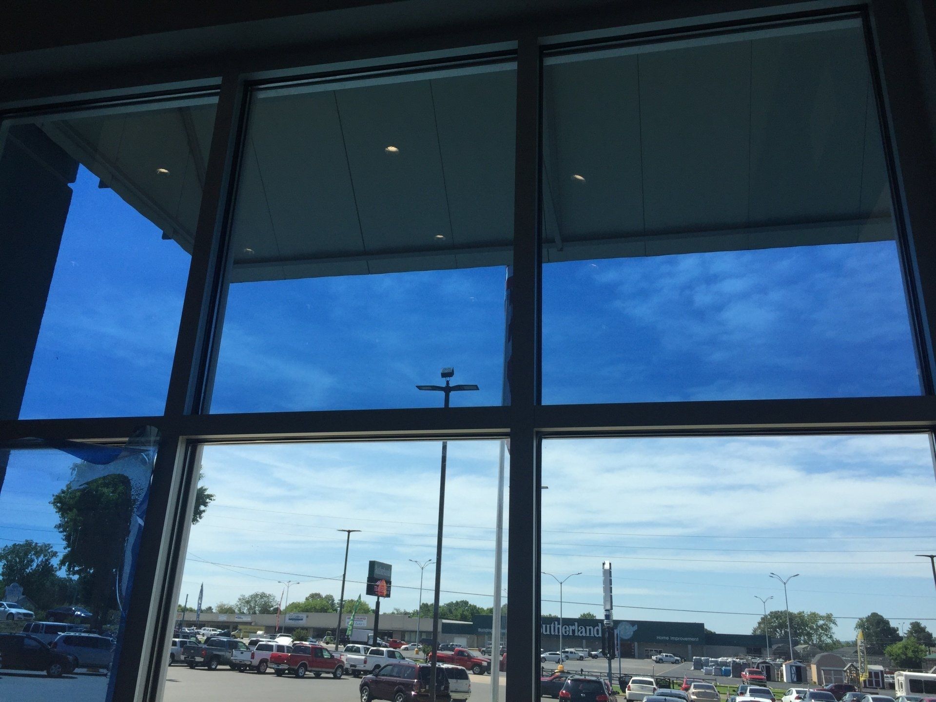 Blue-tinted windows showing a bright sky and a parking lot with cars.