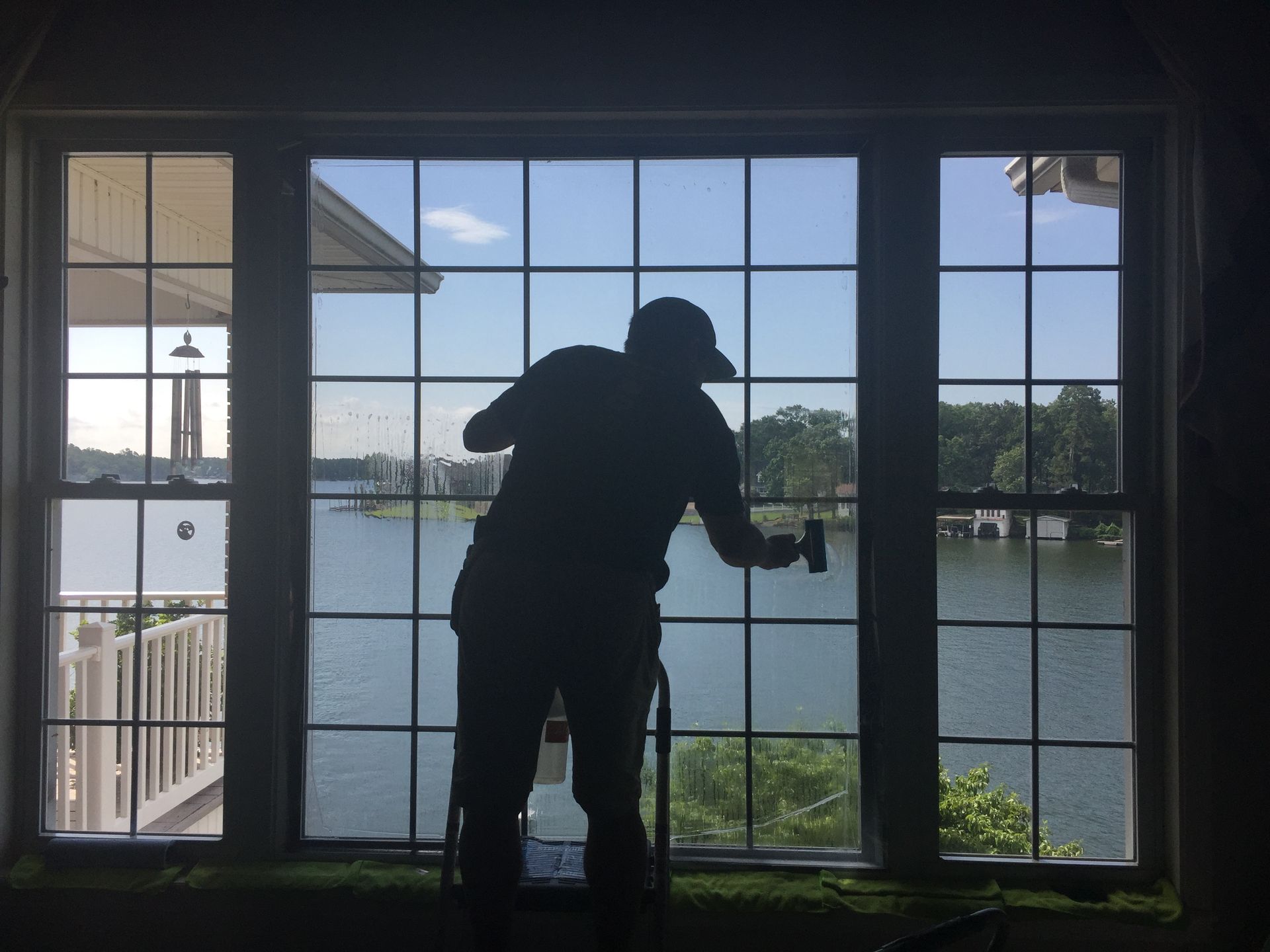 Silhouette of a person cleaning a multi-paned window overlooking a lake.