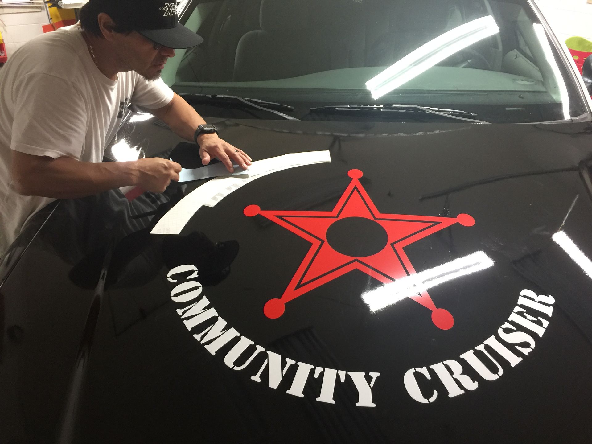 Man applying white decals to the black hood of a car with a 