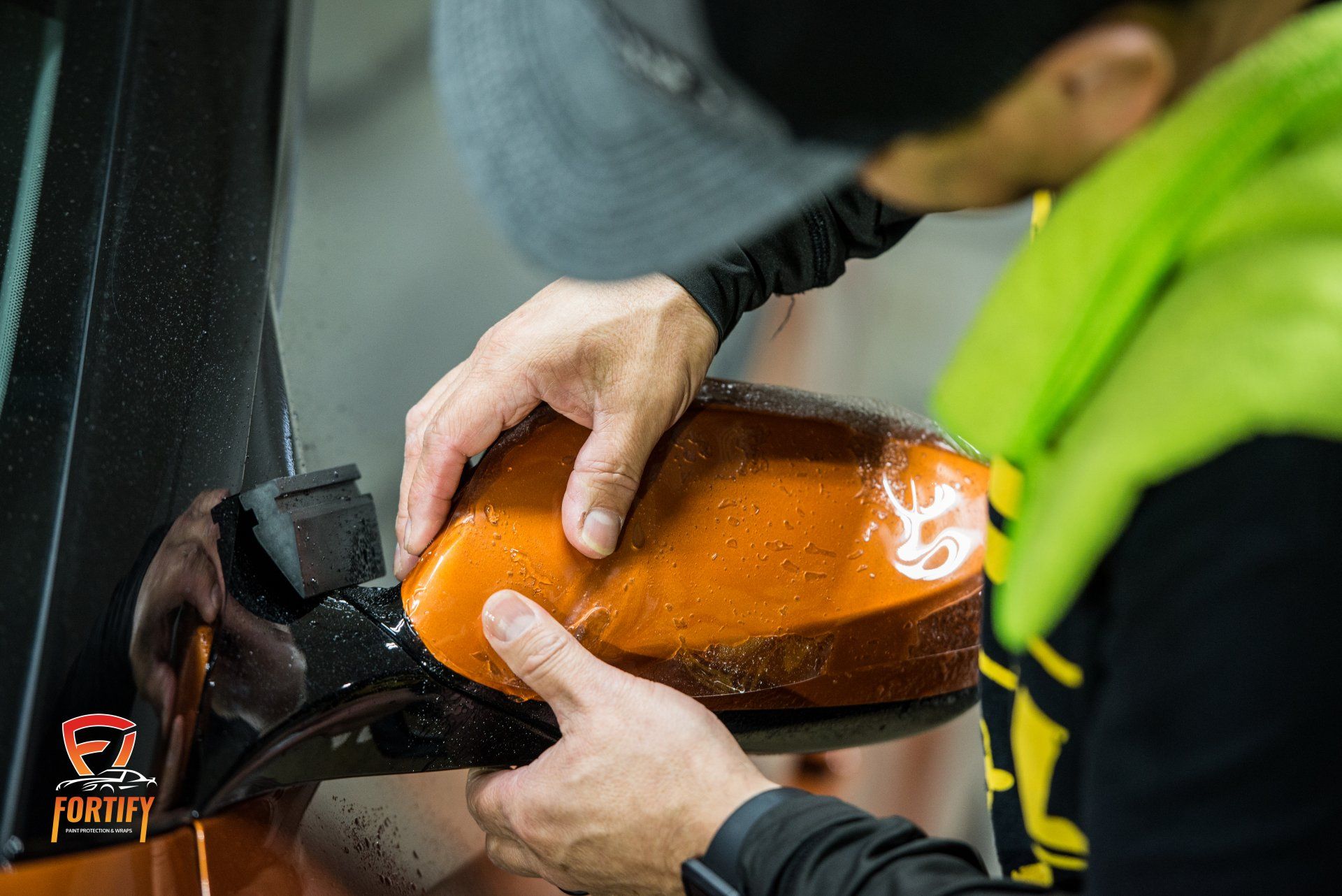 Person applying orange film to a black car side mirror.