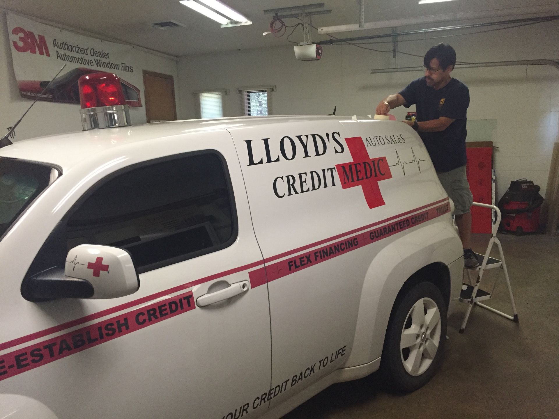 Man on a step stool applying decals to a white van with 