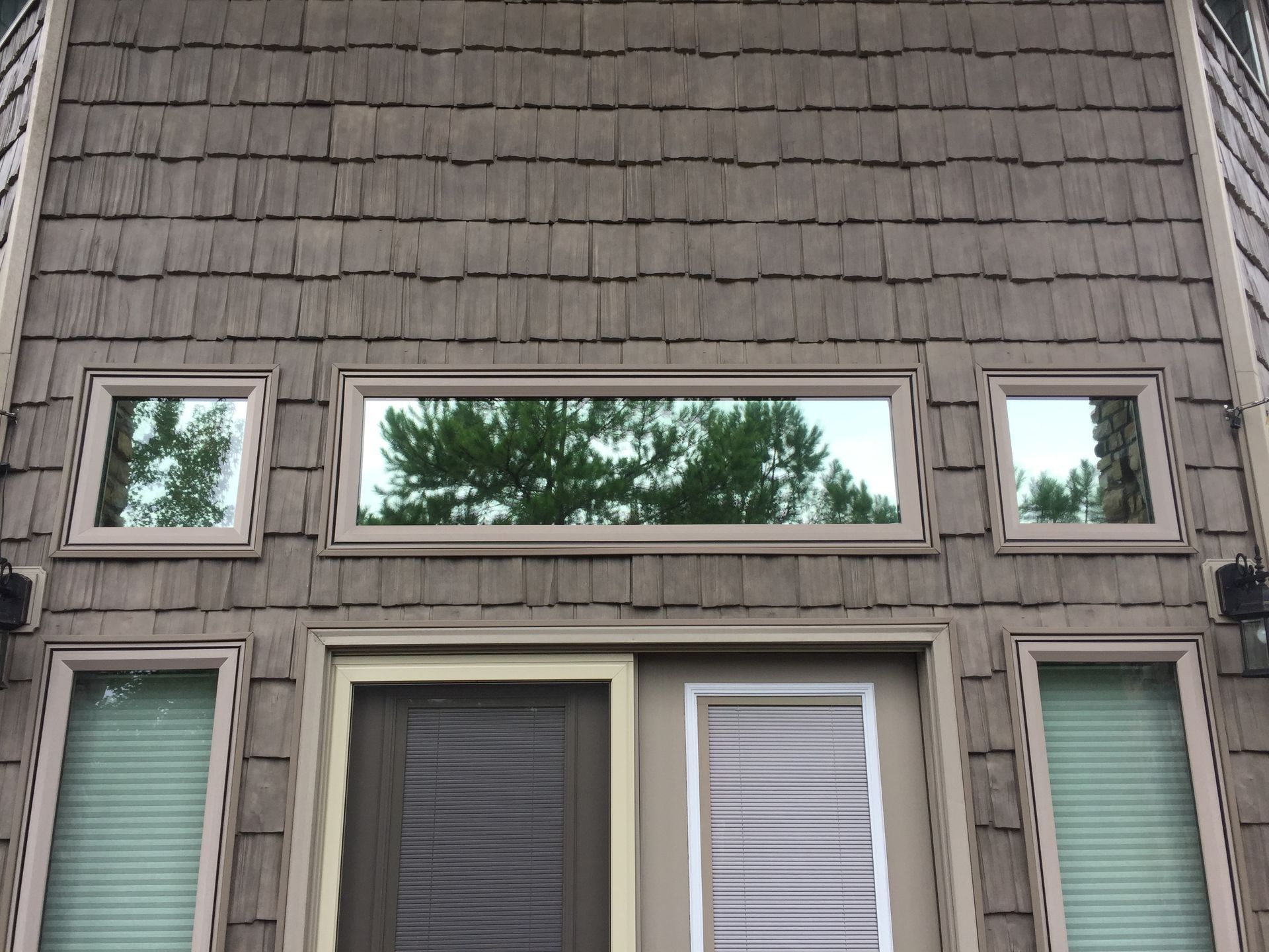 Brown shingle exterior with windows and doors, tan trim. Trees reflect in the upper windows.