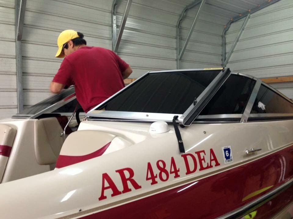 Person working on a boat windshield in a garage, boat is white with red accents.