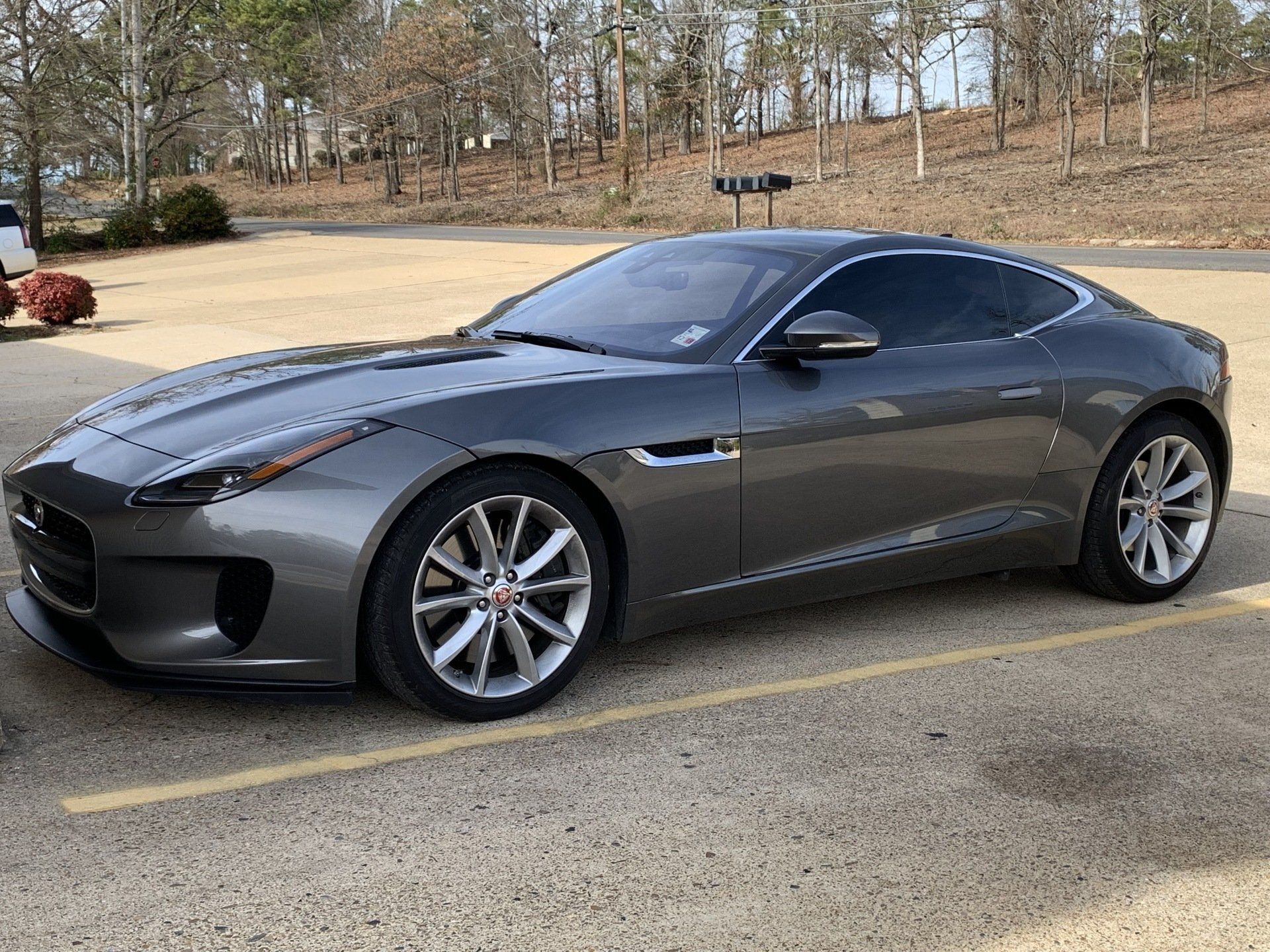 Gray Jaguar F-Type coupe parked in front of a building on a sunny day.