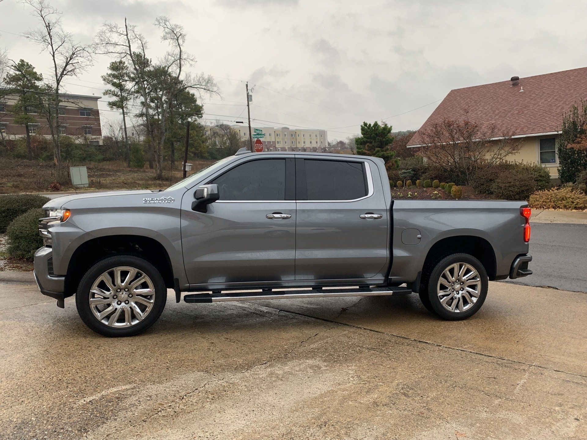 Gray Chevrolet Silverado pickup truck parked on a wet surface in front of buildings.